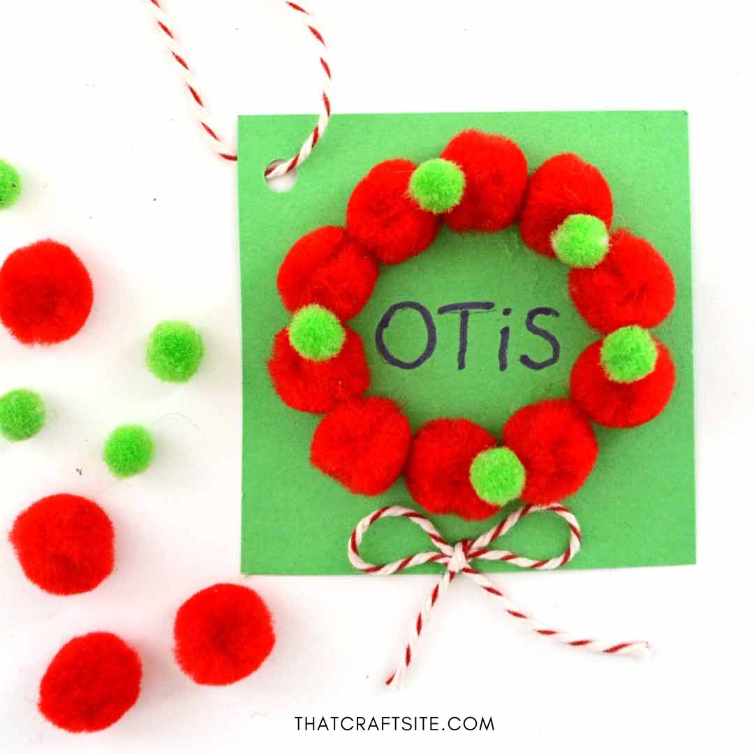 DIY mini pom pom wreath gift tag. Step 6: Use marker to write name and add string through hole in corner. thatcraftsite.com.