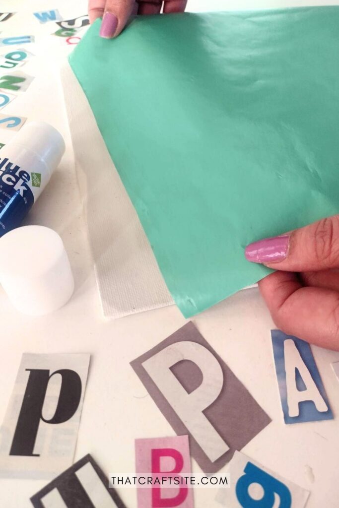 Hands placing green wrapping paper on the canvas. Cut out paper letters on the table around it.