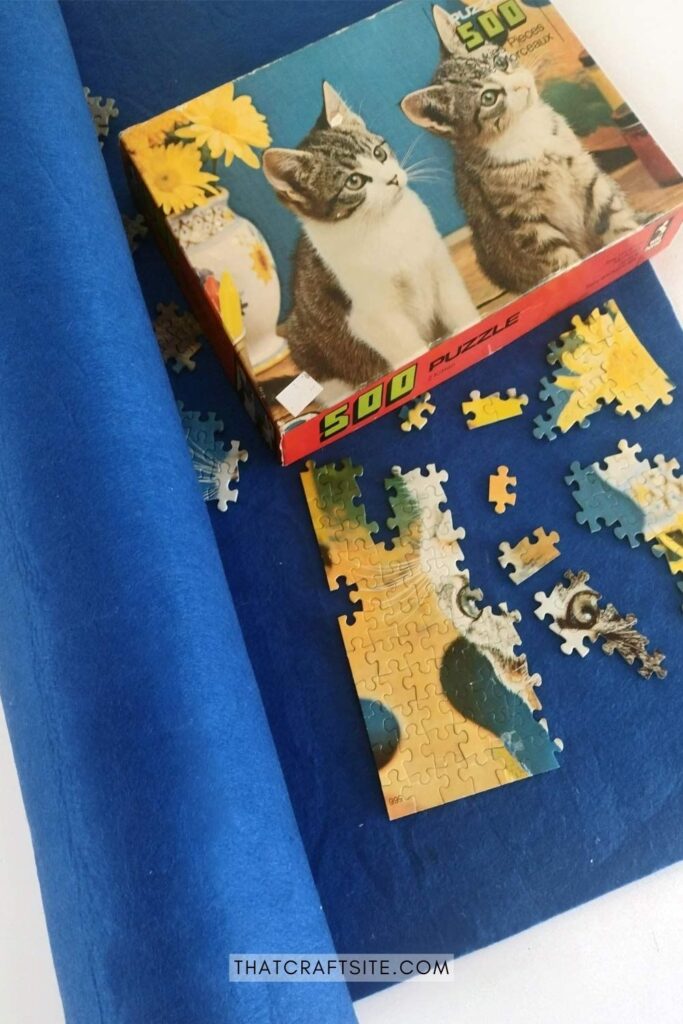 Cat jigsaw puzzle in progress with the box next to it on top of a blue felt puzzle mat.